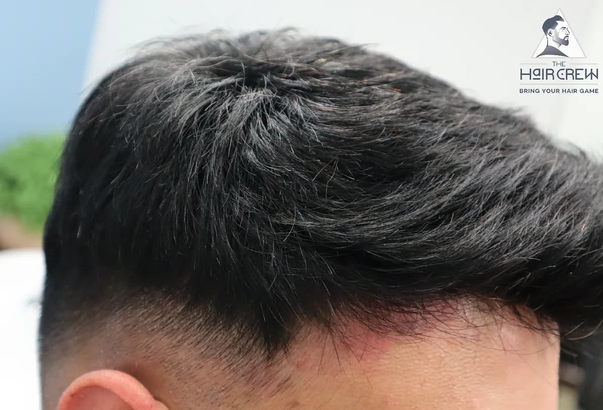 Side view of a client's short dark hair system with a clean cut